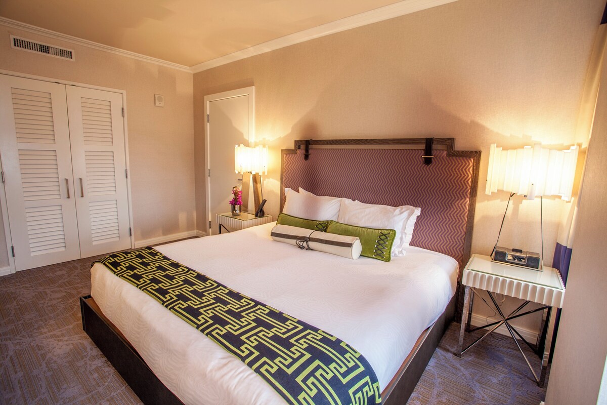 A neatly made bed with a patterned bedspread, a bedside table with a lamp, and a wall-mounted mirror.