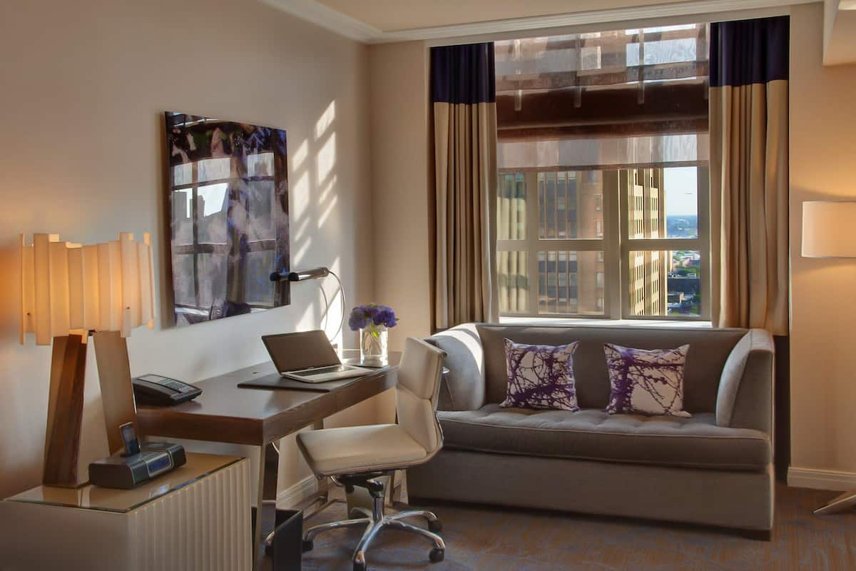 Una camera d'albergo con scrivania, sedia, divano e un'ampia finestra con tende.