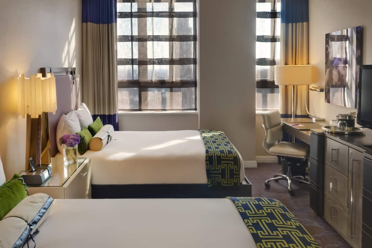 Camera d'albergo con due letti, una scrivania, una sedia, una televisione e una finestra con tende.