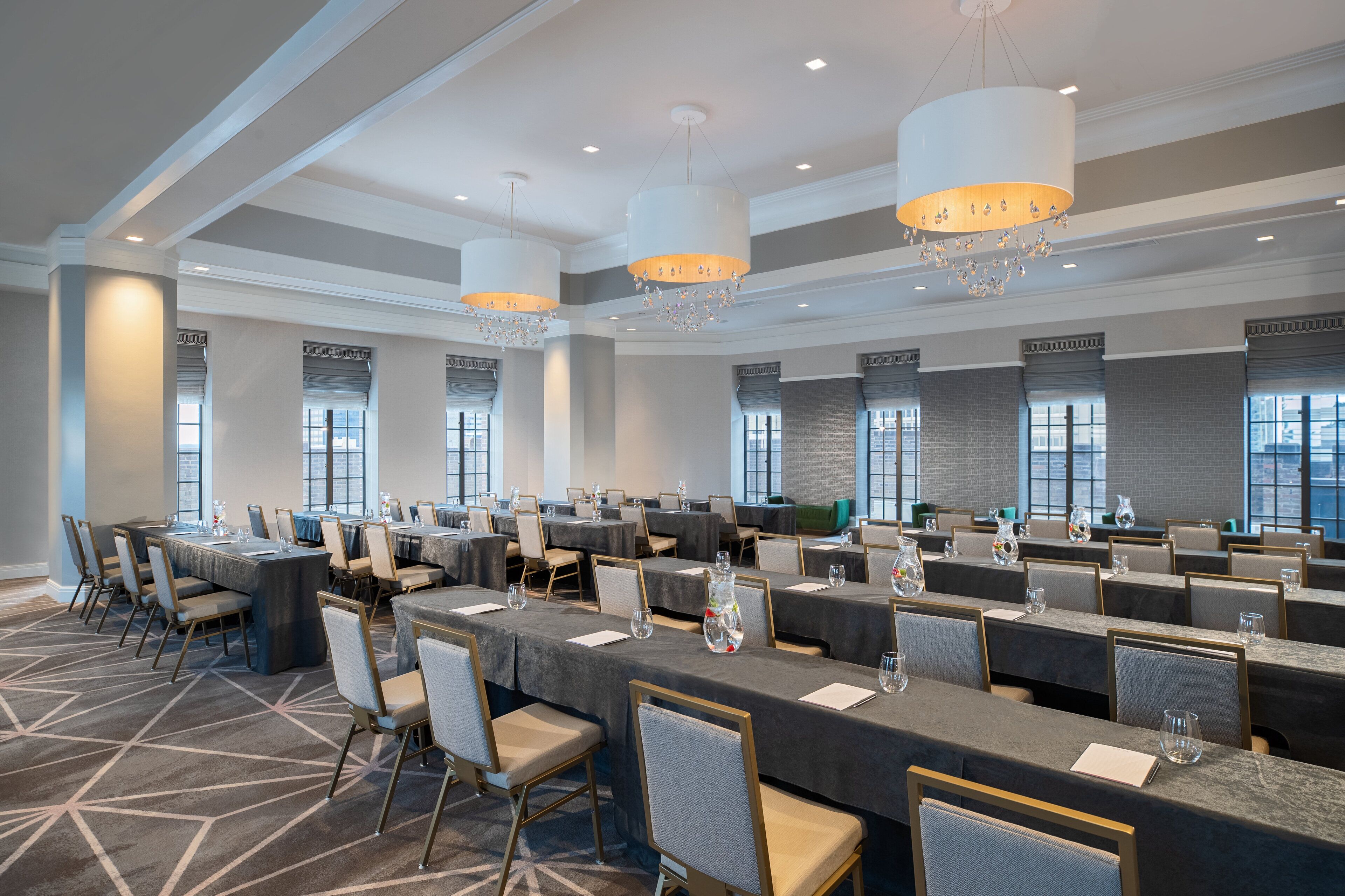 A conference room with multiple tables and chairs, large windows, and chandeliers.