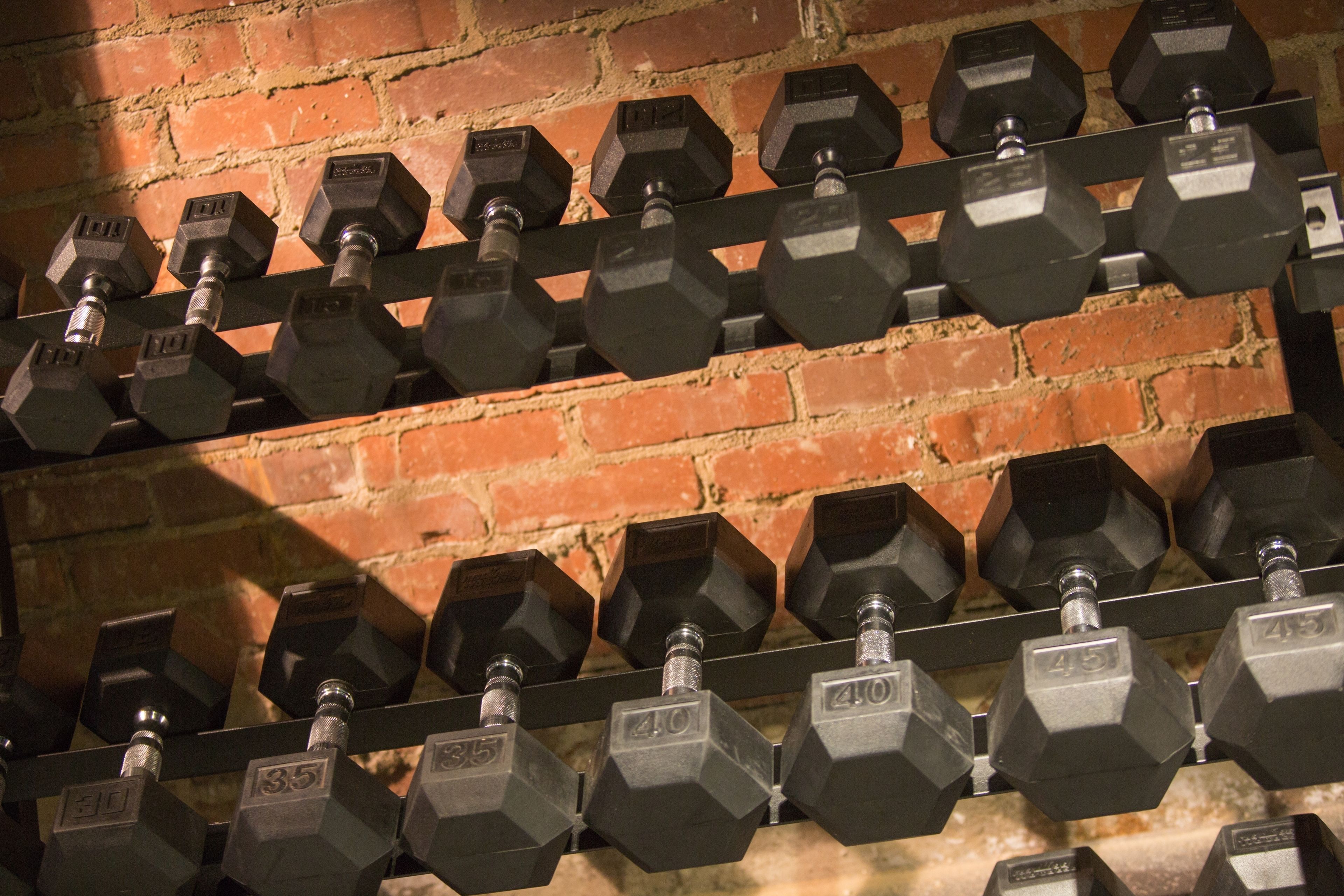 A rack of hexagonal dumbbells with weights ranging from 10 to 45 lbs, arranged against a brick wall.