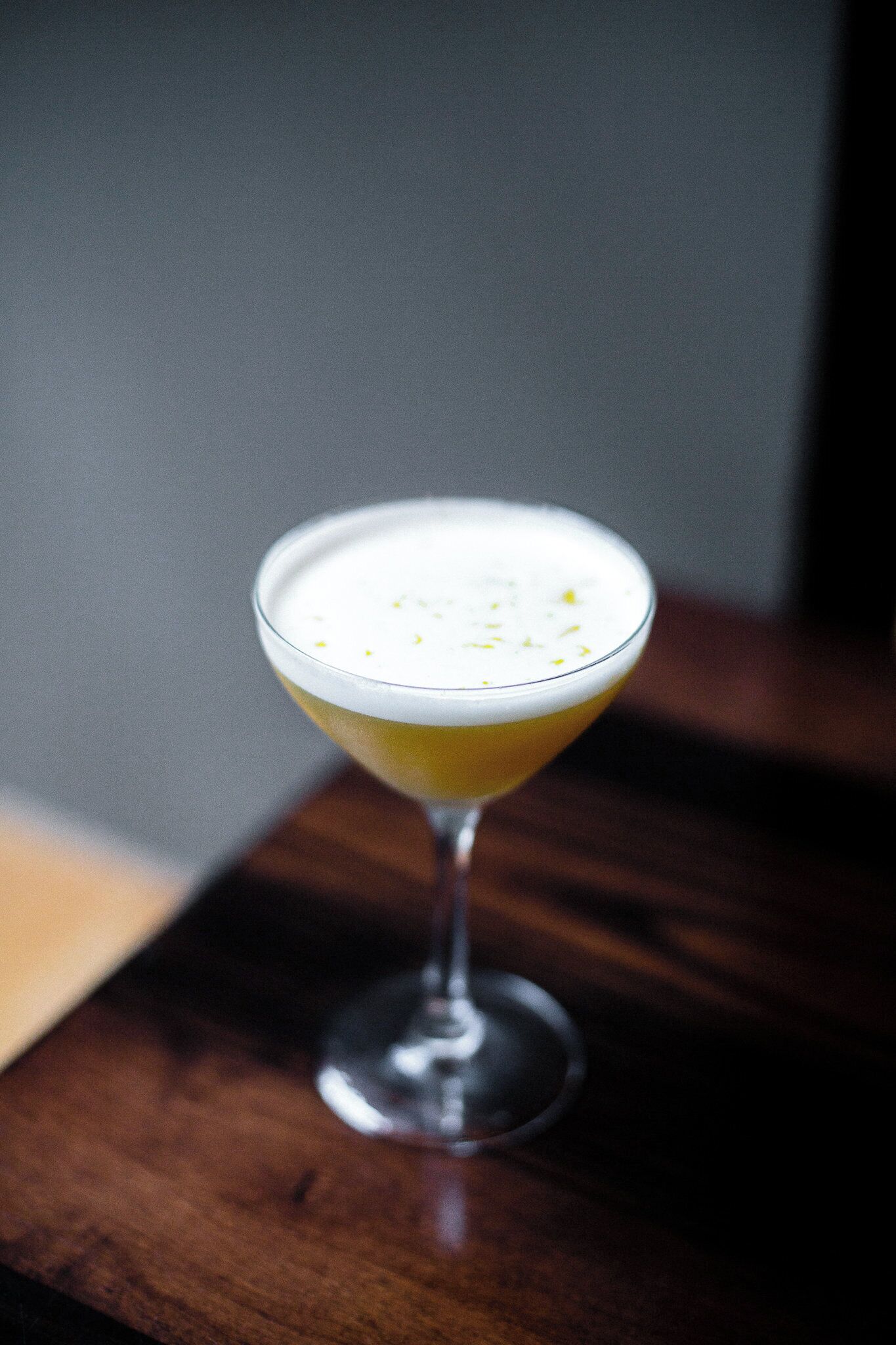 A cocktail in a stemmed glass on a wooden surface.