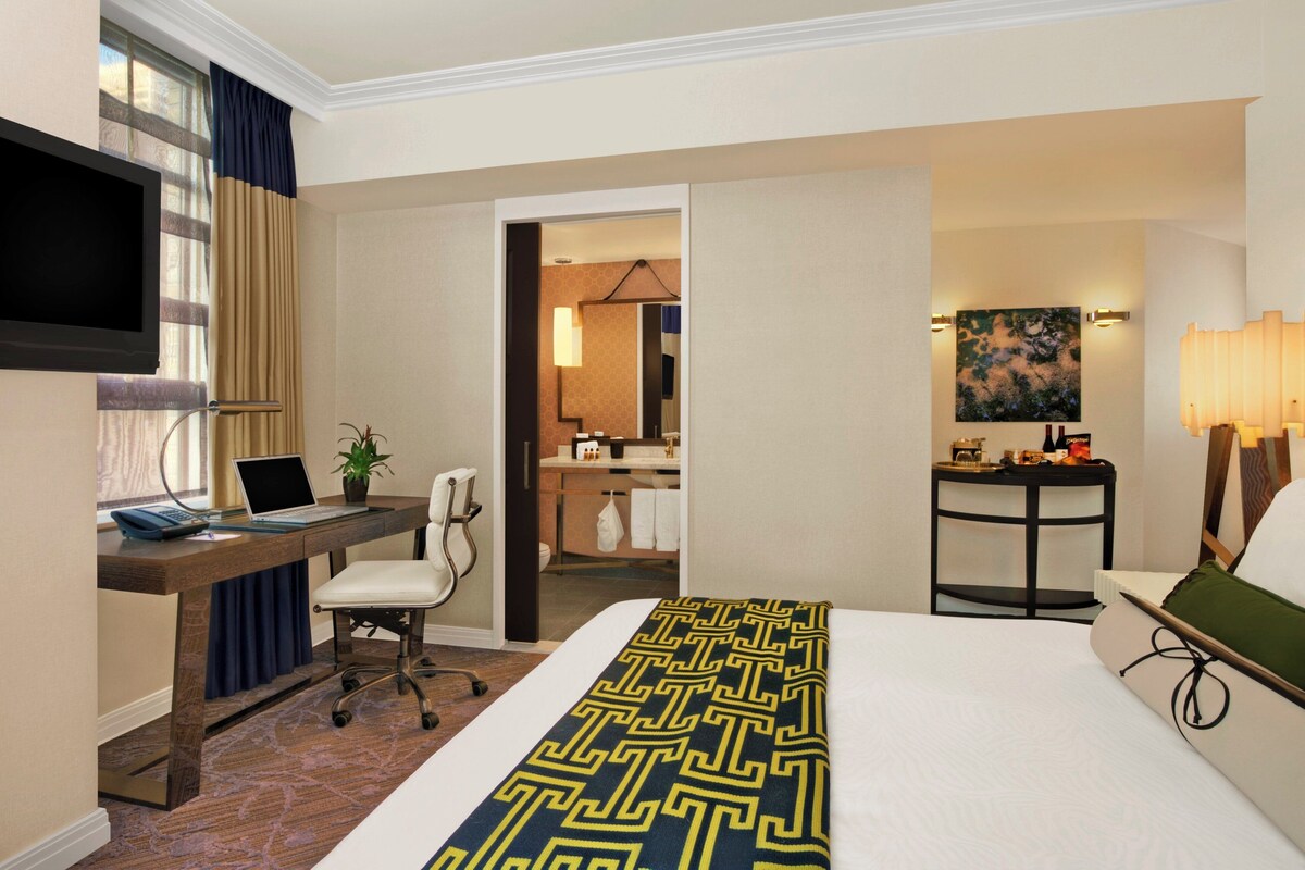 A hotel room with a bed, desk, chair, TV, and a bathroom visible through an open door.