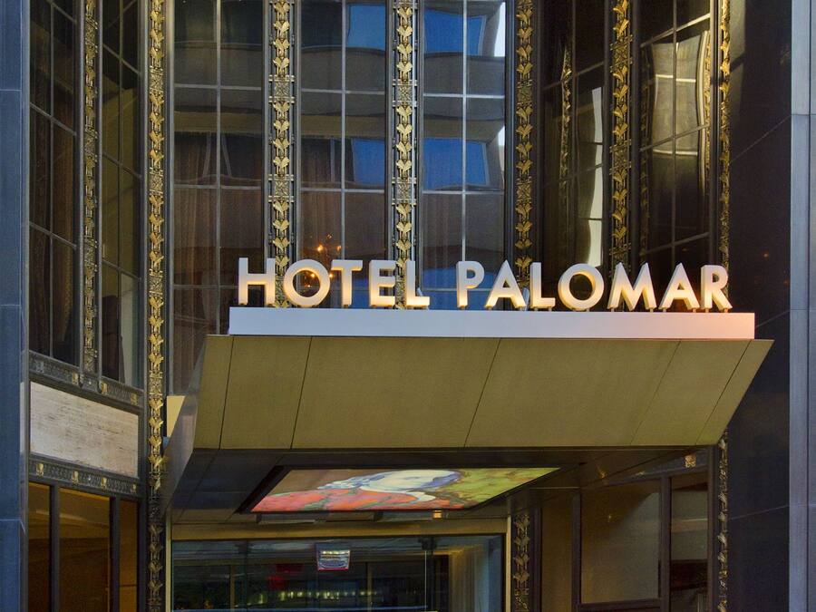 The entrance of Hotel Palomar with a modern facade, large glass windows, and a prominent sign above the entrance.