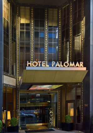 L’entrée de l’hôtel Palomar se distingue par sa façade moderne, ses grandes fenêtres en verre et une enseigne bien visible au-dessus de la porte.