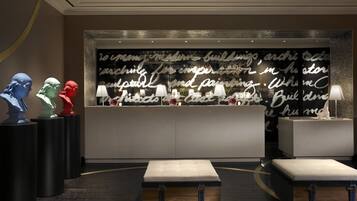 A reception area with a modern design, featuring a large wall with artistic text, three sculptural busts, and two illuminated lamps.