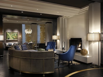 A modern living room with a grey armchair, a small side table with a bottle and glasses, a bookshelf with various items, and a window providing natural light. at Kimpton Hotel Palomar Philadelphia by IHG
