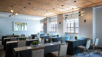 Un salón de conferencias con mesas dispuestas para reuniones, equipado con sillas y decorado con pequeñas plantas y cristalería.