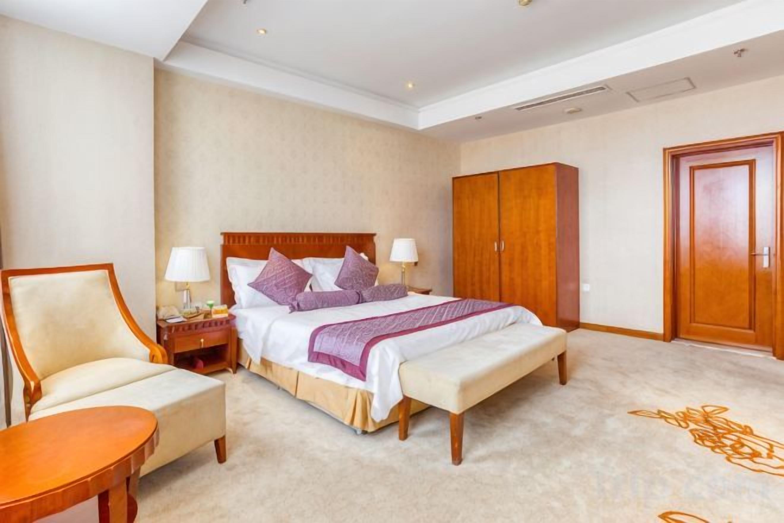 Quarto de hotel com cama, mesas de cabeceira, uma cadeira, guarda-roupa e chão coberto por carpete.