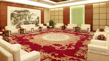 Un salón de conferencias con alfombra roja grande, sillas blancas y un cuadro grande en la pared.