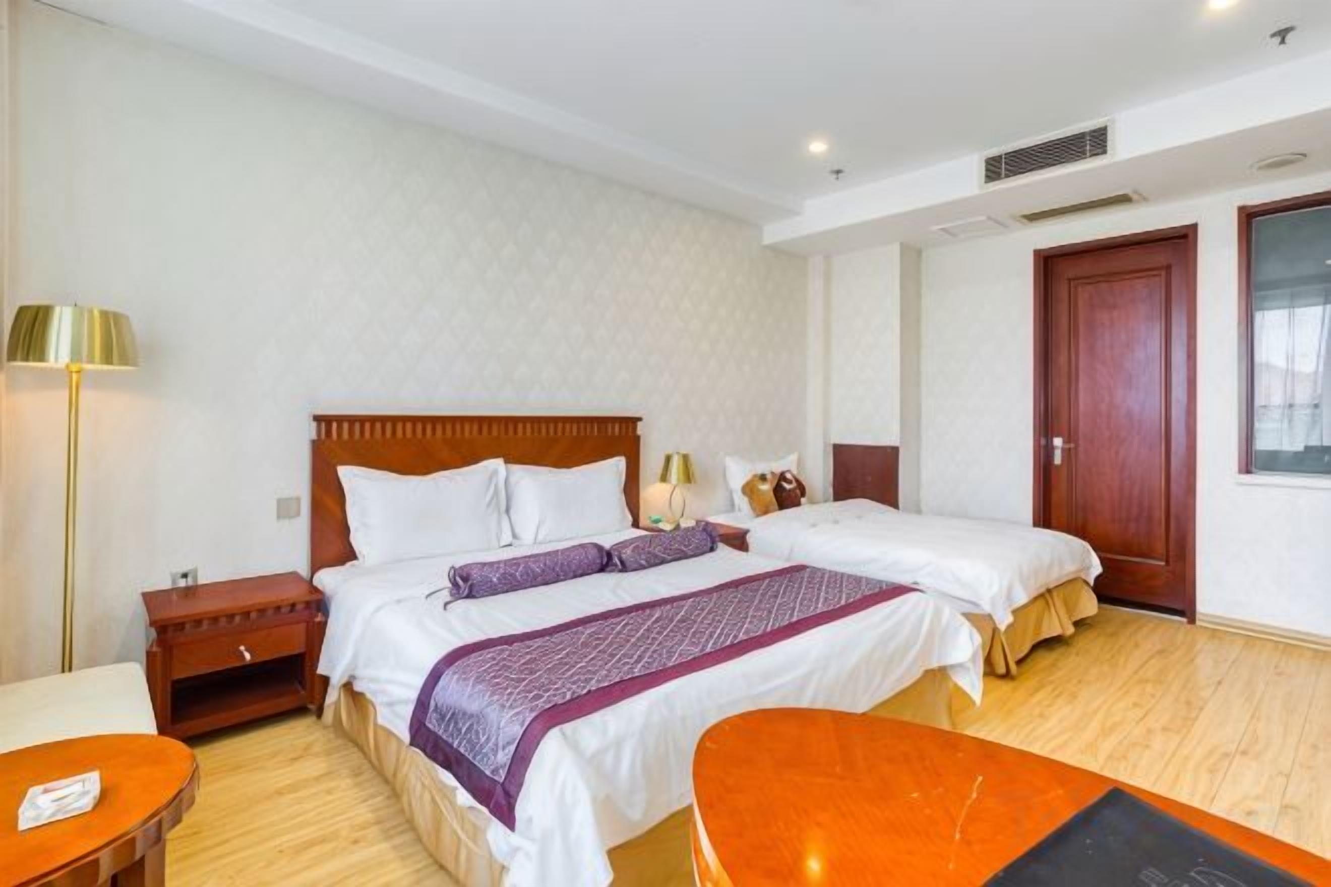 Una habitación de hotel con dos camas, un escritorio, una silla, una lámpara y una puerta.