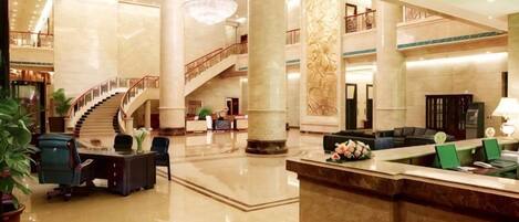 A spacious lobby with a marble reception desk, a staircase, and a chandelier.