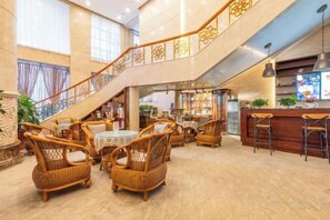 A hotel lobby with wicker furniture, a staircase, and a bar area. - Petroleum Hotel (Jinzhou)