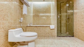 Un baño con inodoro, cabina de ducha de vidrio y paredes de mármol.