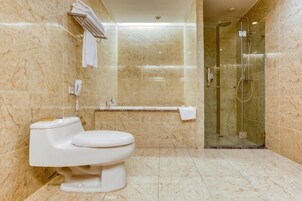 Un baño con inodoro, cabina de ducha de vidrio y paredes de mármol.
