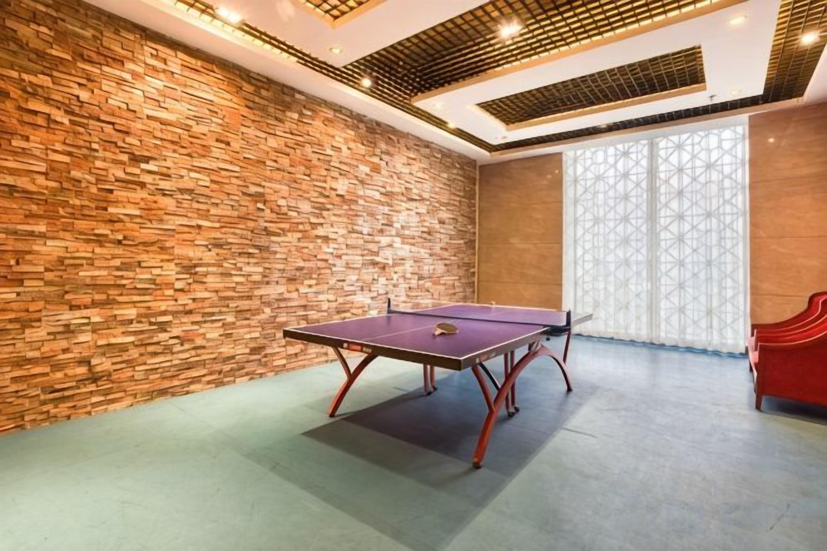 A ping pong table in a room with a brick wall and a large window with a geometric pattern.