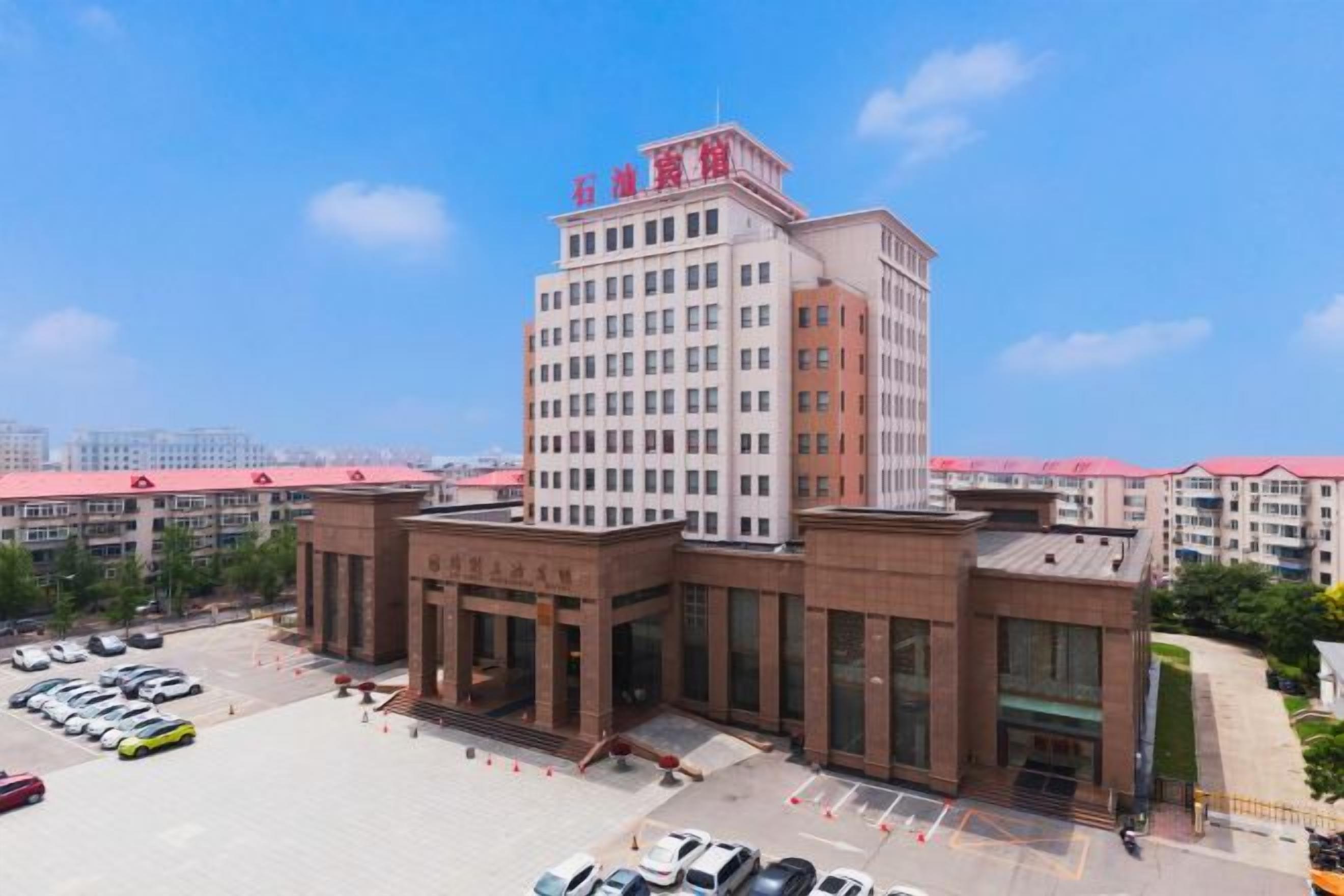 A multi-story hotel with a central entrance, a parking lot, and a clear sky.