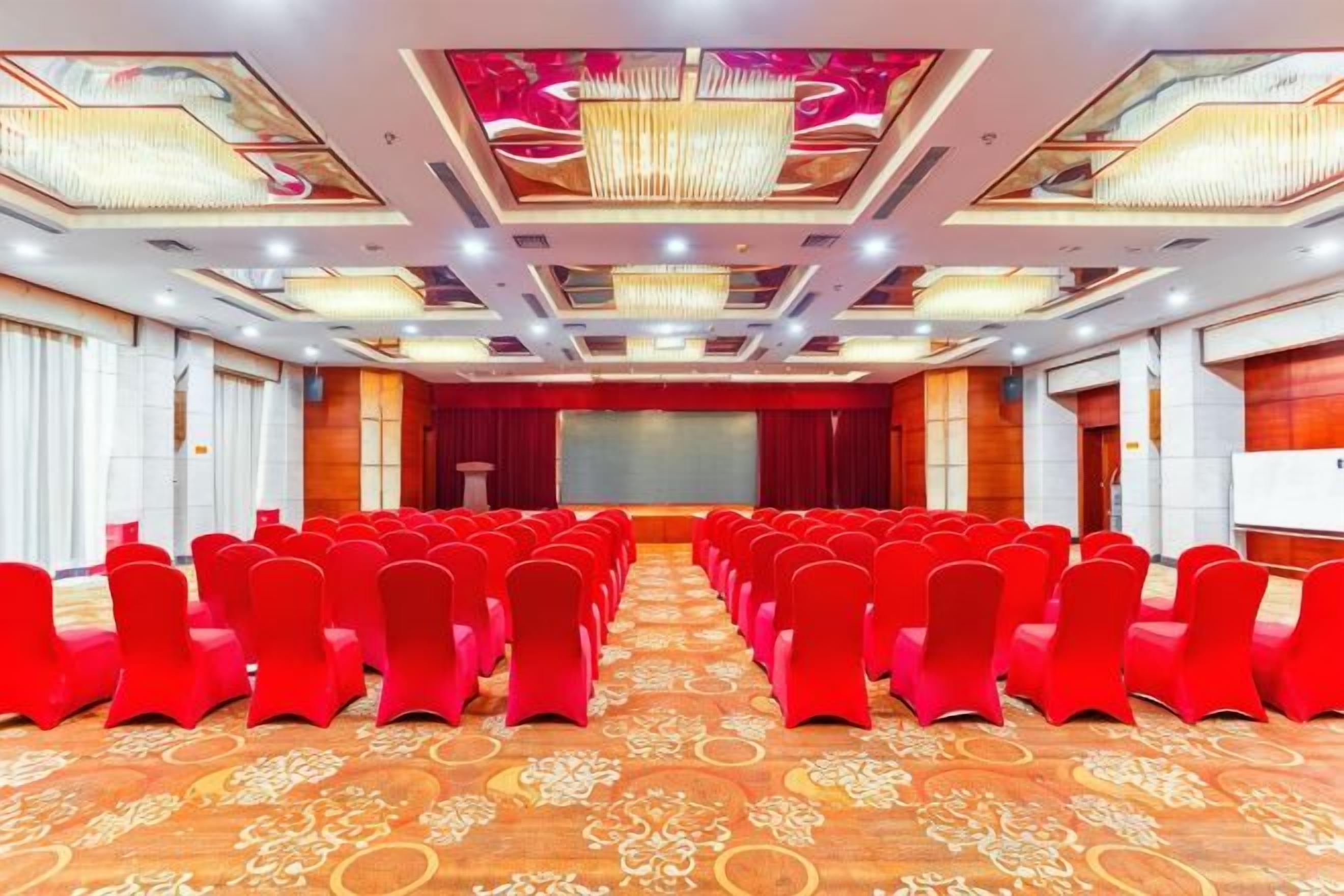 A conference room with rows of chairs, a stage, and a large screen.