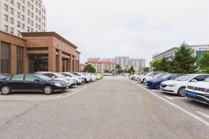 A parking lot with multiple cars parked in rows, a building with a red roof in the background, and a clear sky. - Petroleum Hotel (Jinzhou)