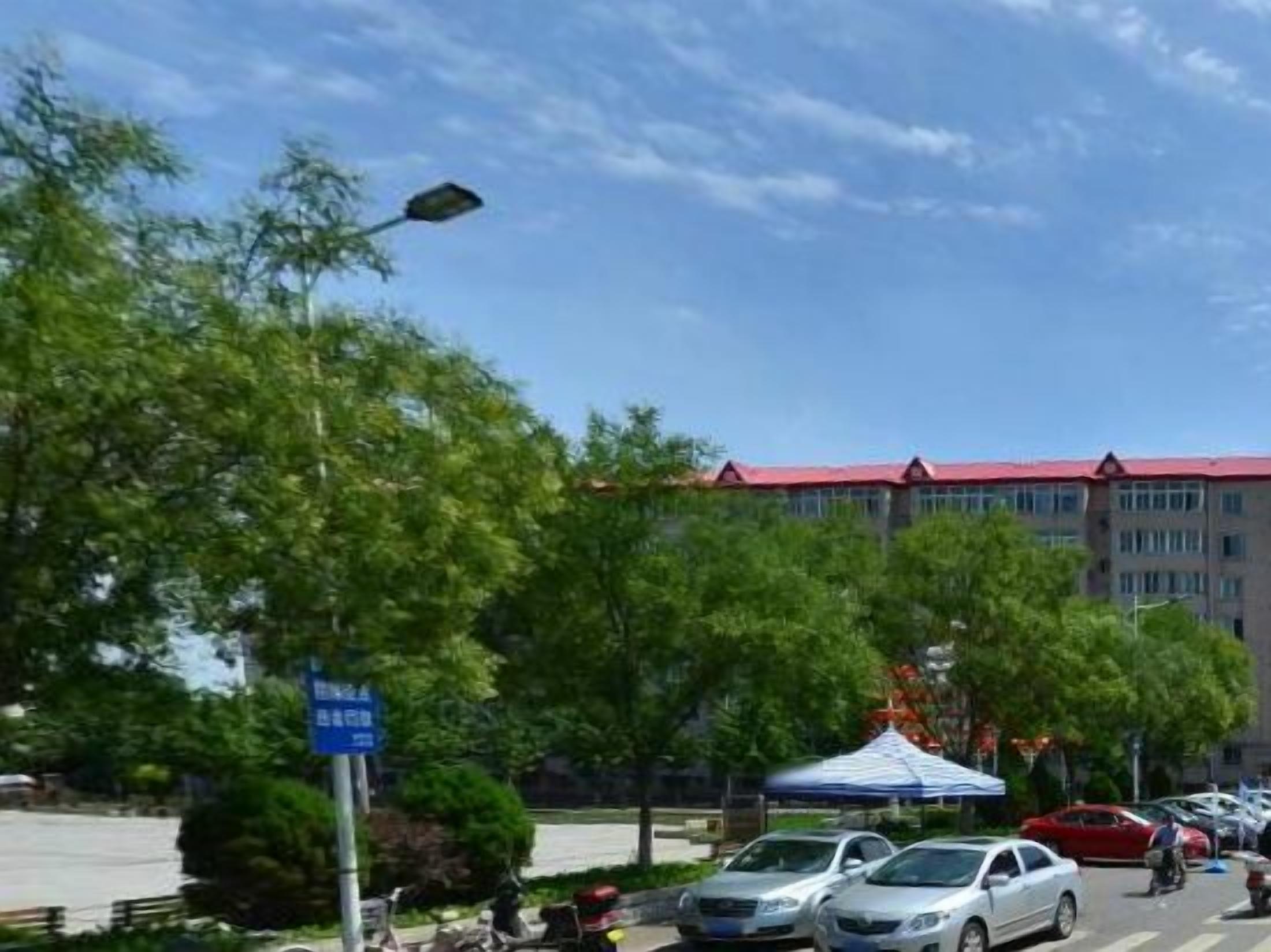 A street scene with parked cars, a blue sign, and a building with a red roof.