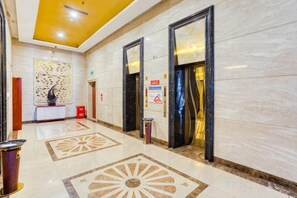 Vestíbulo de hotel con piso de mármol, una recepción y dos ascensores.