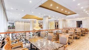 A spacious dining area with a long table and multiple chairs, a decorative light fixture, and a wooden floor.