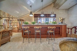 Uma área de bar com banquetas de madeira, balcão e iluminação pendente.