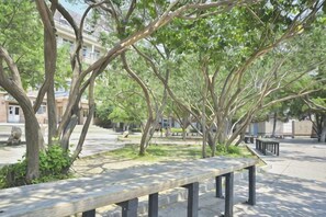 A park bench in a shaded area with trees and a building in the background. - Petroleum Hotel (Jinzhou)