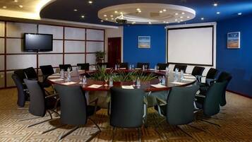 Una sala de conferencias con una mesa redonda, sillas, una pantalla de proyector y un televisor.