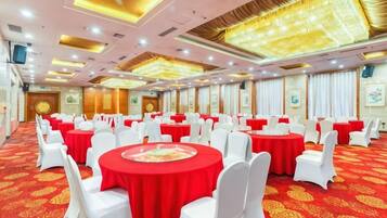 Un salón de banquetes con mesas redondas, sillas blancas y manteles rojos.