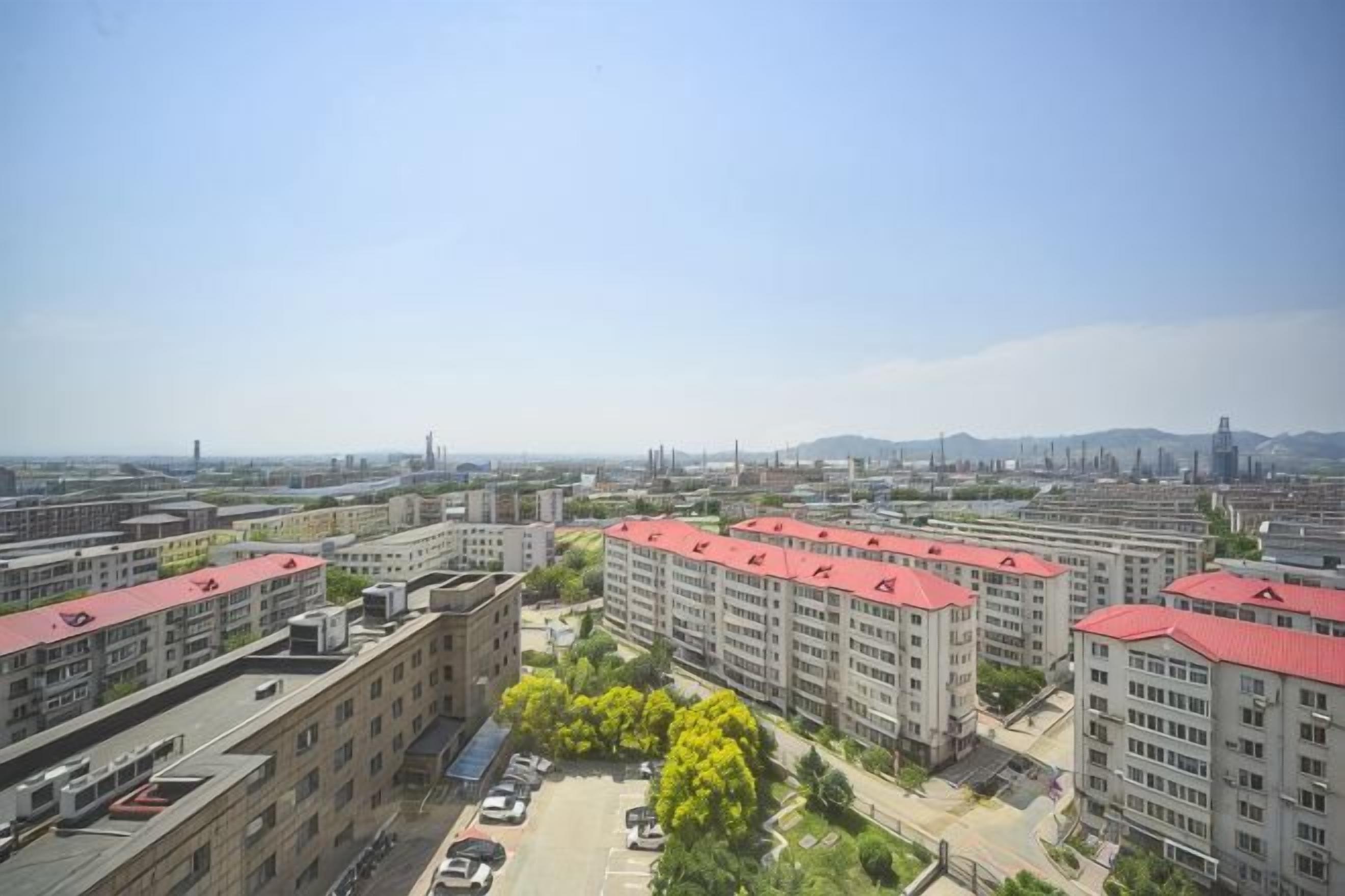 Ett högt bostadskomplex med flera bostadshus, en parkeringsplats och en klar himmel.