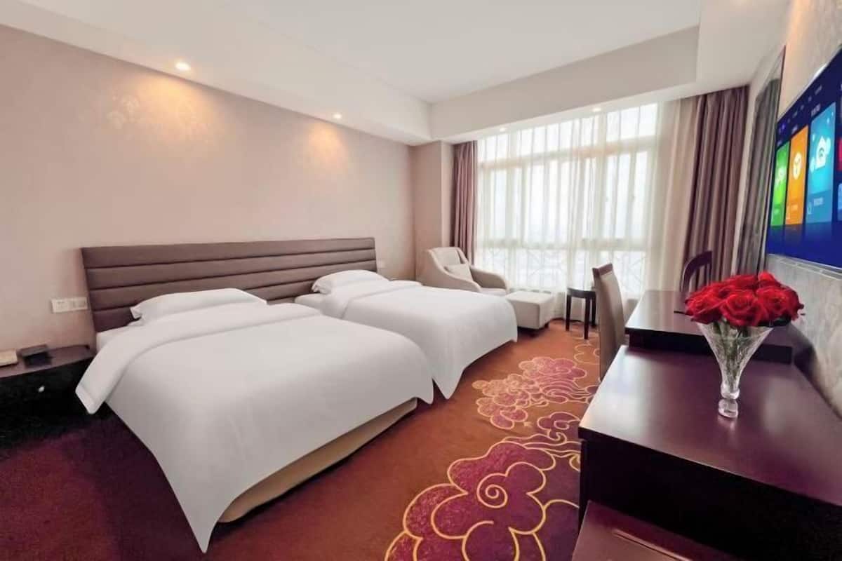 Habitación de hotel con dos camas, un escritorio, una silla y un ventanal con cortinas.