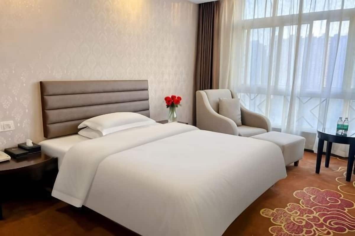 Habitación de hotel con una cama grande, una silla, una mesita de noche y una mesa con un jarrón de flores.