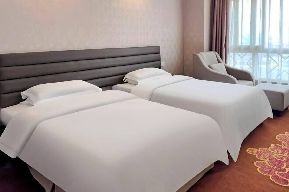 Habitación de hotel con dos camas, una silla y vistas a la ciudad.