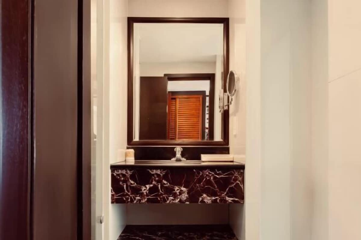 Een badkamer met een marmeren wastafelmeubel, een spiegel en een houten deur op de achtergrond.