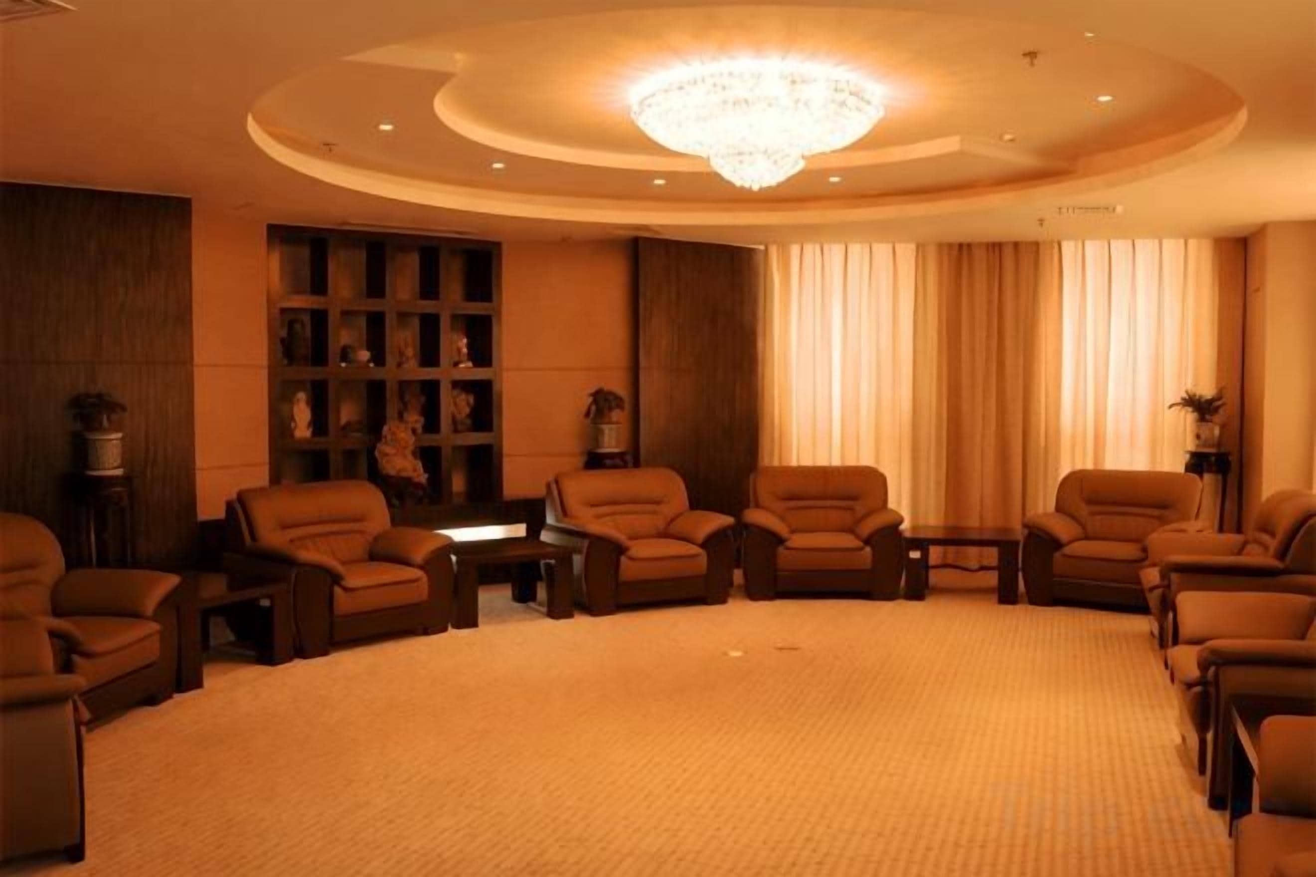 Uma área de estar circular com sofás e uma mesa central, cercada por um piso coberto de carpete e um candelabro.