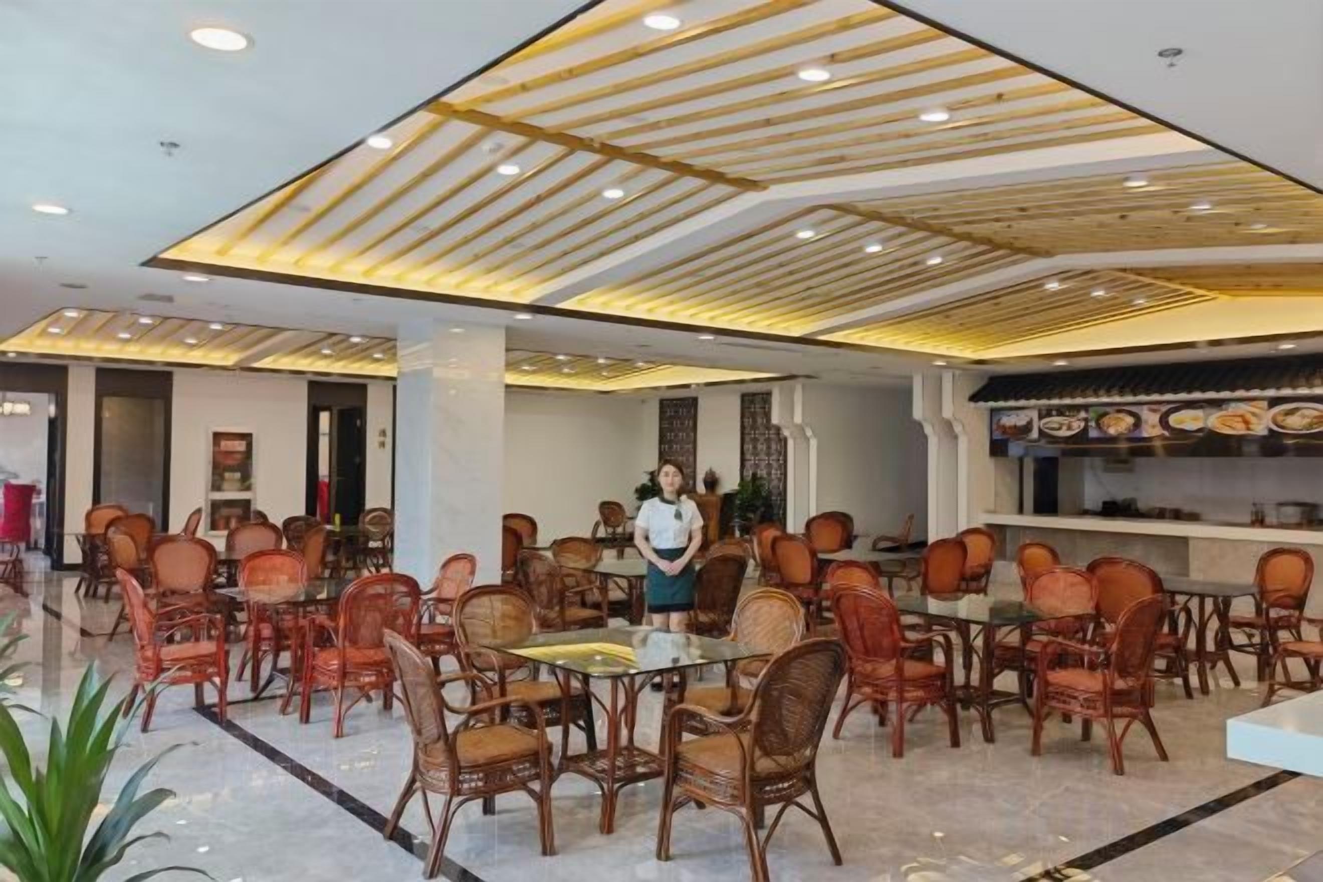 A spacious dining area with multiple tables and chairs, a modern ceiling design, and a visible kitchen area.