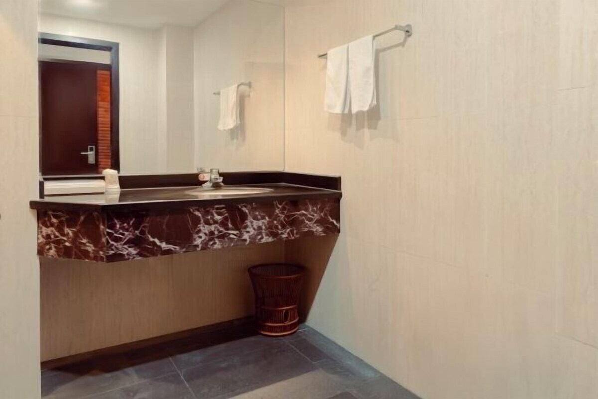 Een badkamer met een marmeren wastafel, een spiegel, een handdoekrek en een prullenbak.