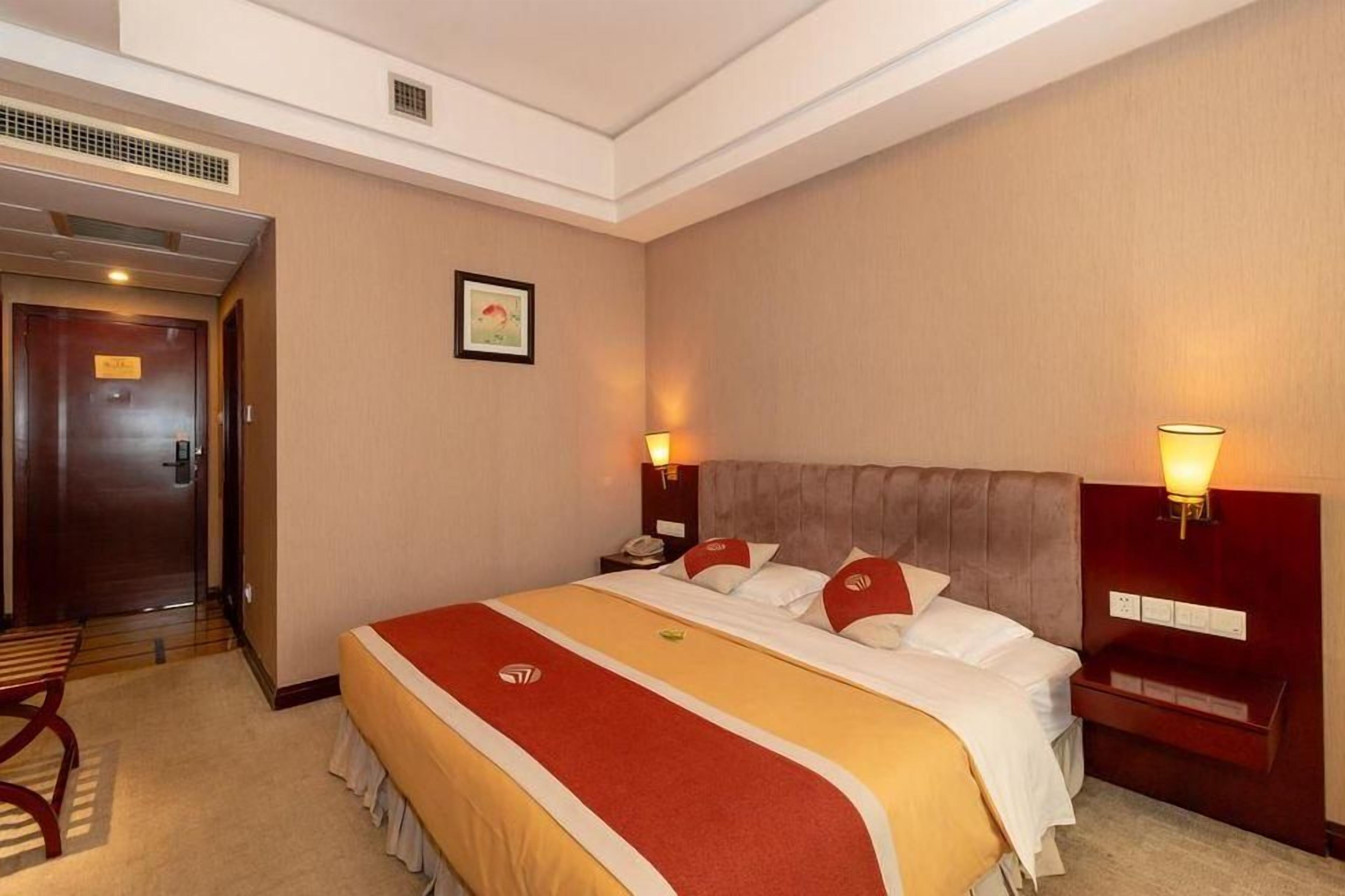 Ein Hotelzimmer mit einem großen Bett, zwei Nachttischen, einem Kopfteil und einer Tür.
