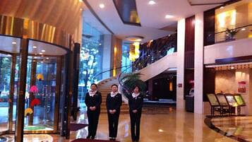 A hotel lobby with a grand staircase, a reception desk, and a glass entrance.