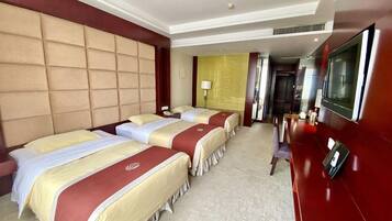 A hotel room with three beds, a TV, and a desk.