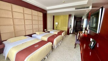 Habitación de hotel con tres camas, televisor y escritorio.