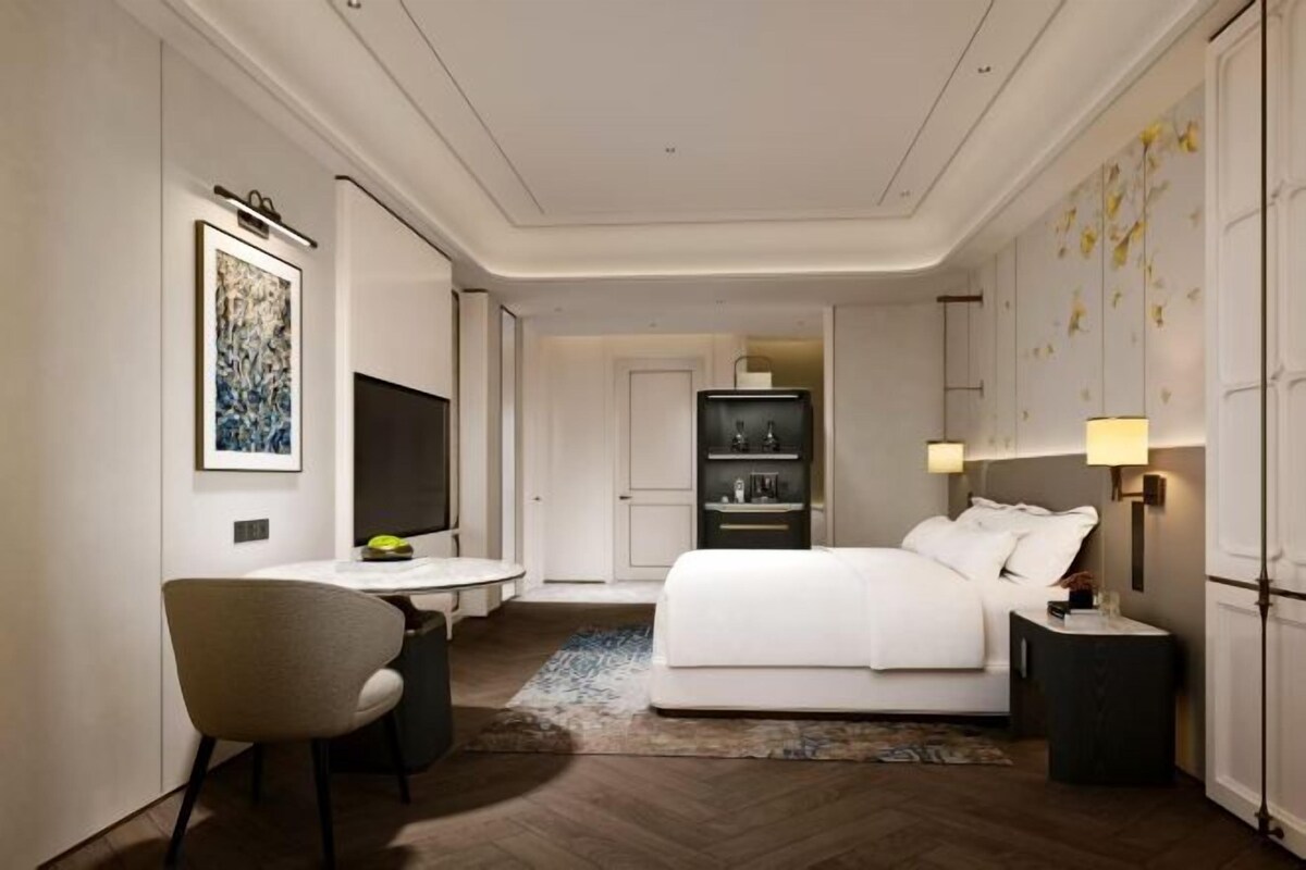 A hotel room with a bed, a desk, a chair, a TV, and a bookshelf.