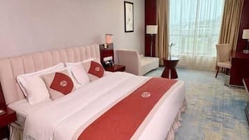 A hotel room with a large bed, a desk, a chair, and a window with curtains.