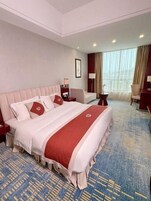 Habitación de hotel con una cama grande, un escritorio, una silla y un ventanal con cortinas.