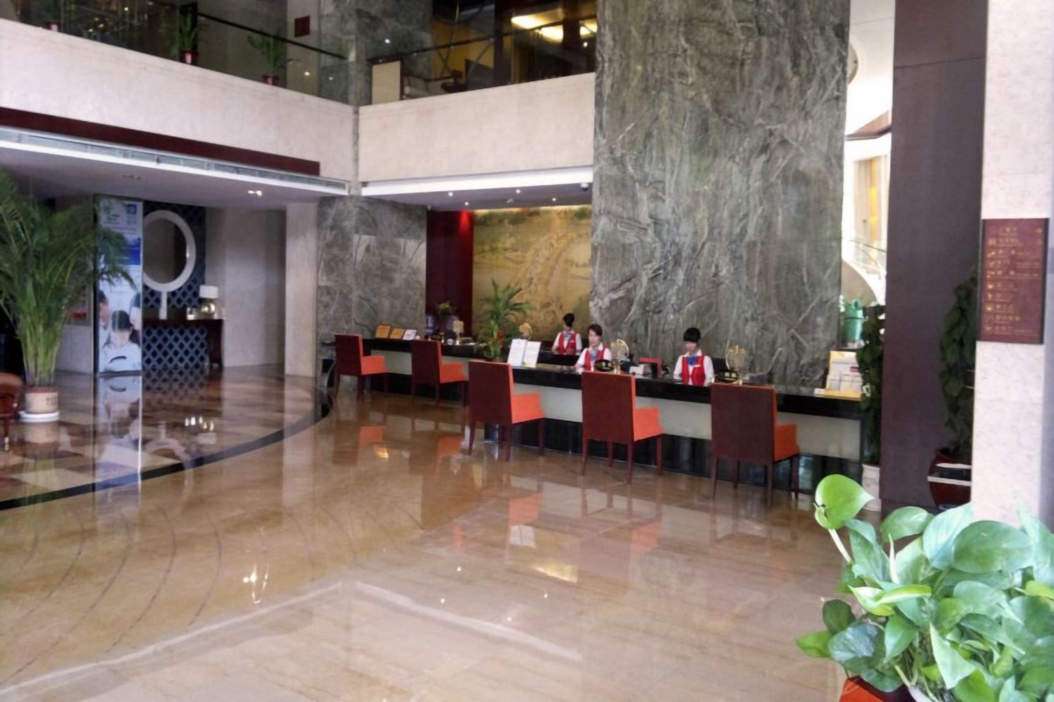A lobby with a marble reception desk, multiple seating areas, and potted plants.