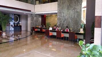 A lobby with a marble reception desk, multiple seating areas, and potted plants.