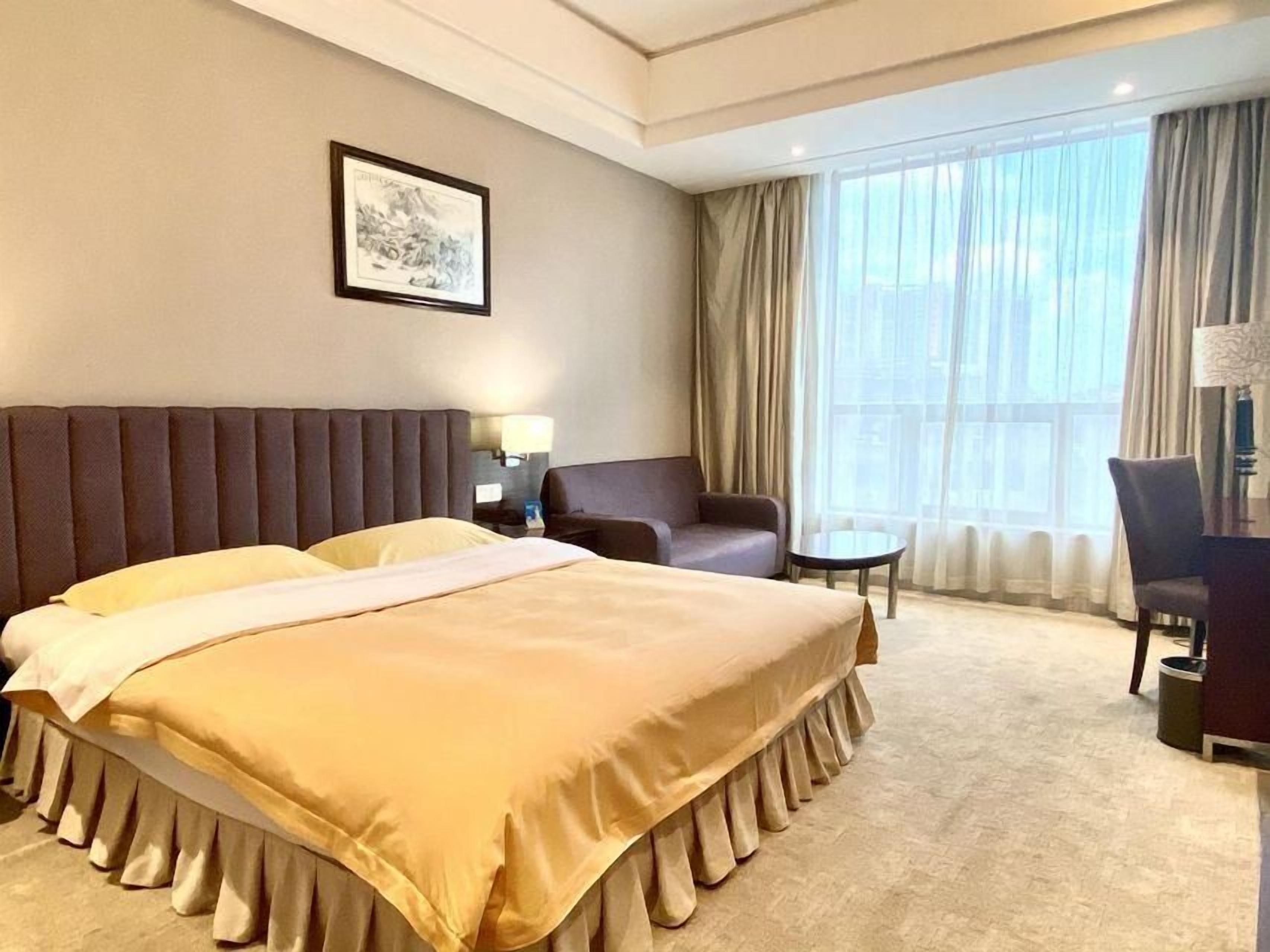 Une chambre d’hôtel avec un grand lit, une chaise, une petite table et une fenêtre avec des rideaux.
