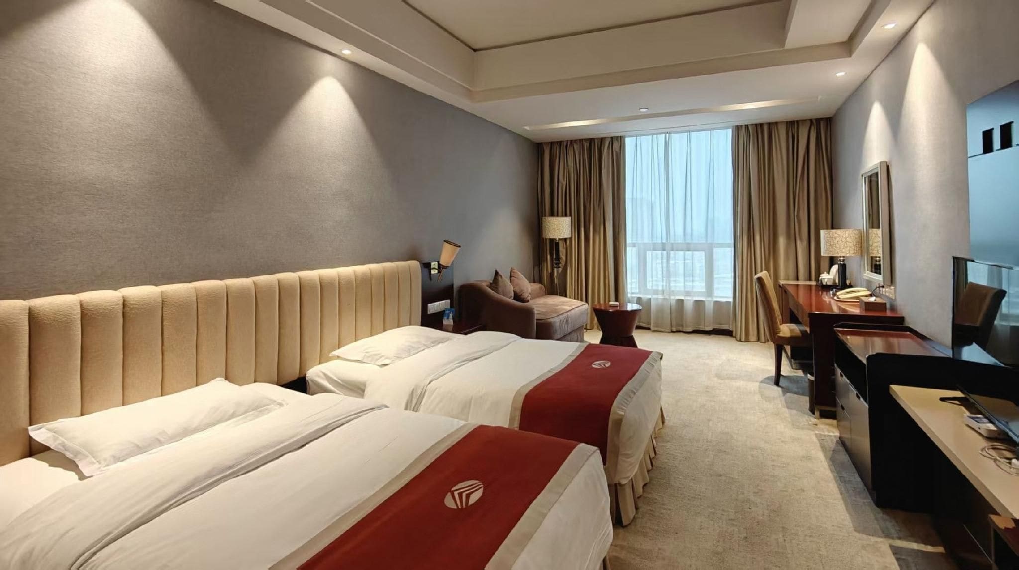 Une chambre d’hôtel avec deux lits, un bureau, une chaise, une télévision et une grande fenêtre avec des rideaux.