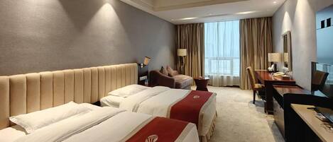 Une chambre d’hôtel avec deux lits, un bureau, une chaise, une télévision et une grande fenêtre avec des rideaux.